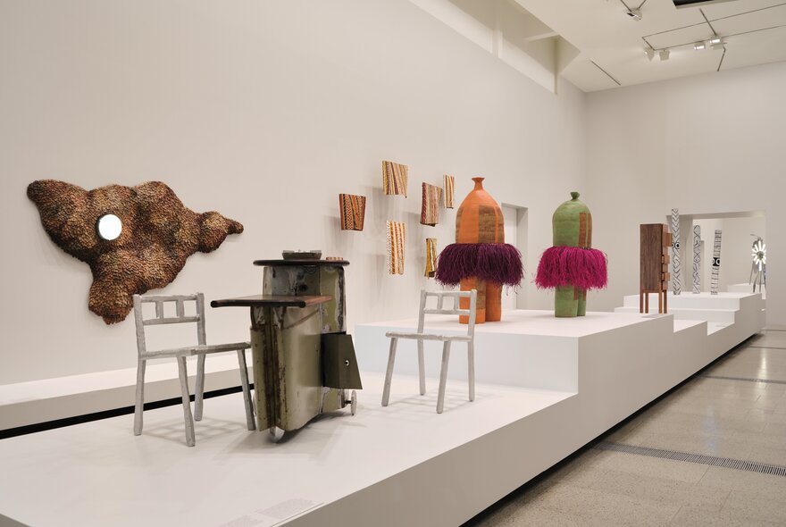 Creative design artworks displayed in a white gallery setting, with some artworks hanging on the wall and others on a white dais.