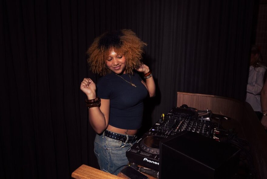 A DJ with big hair dances on the spot.