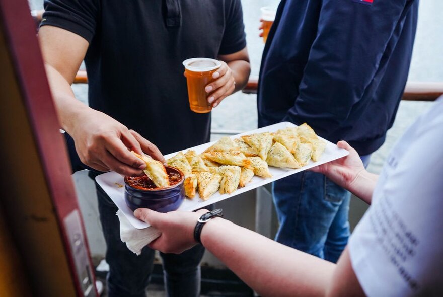 A hand selecting food from a tray of canapes being held out in front of him, on board a boat.