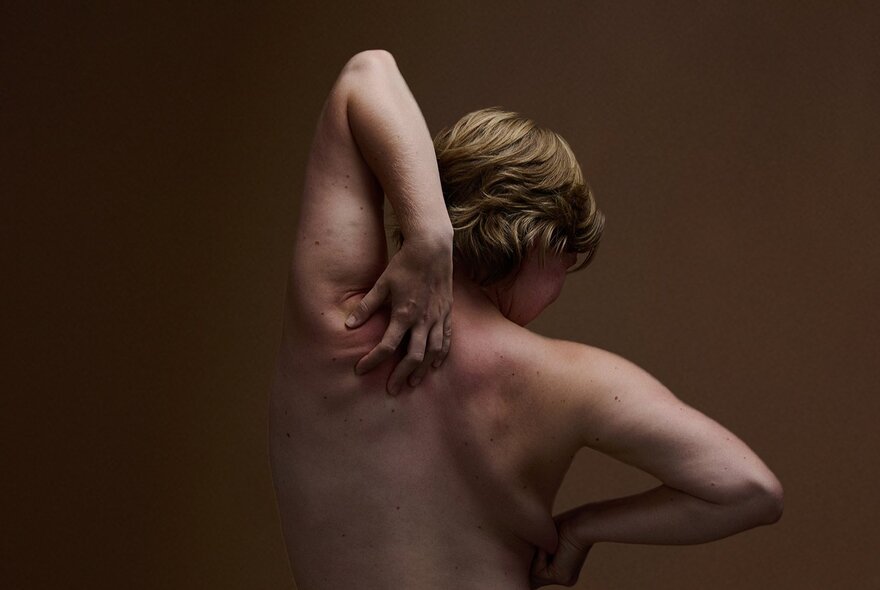 A person with their back to the viewer, reaching over their left shoulder to scratch their back.
