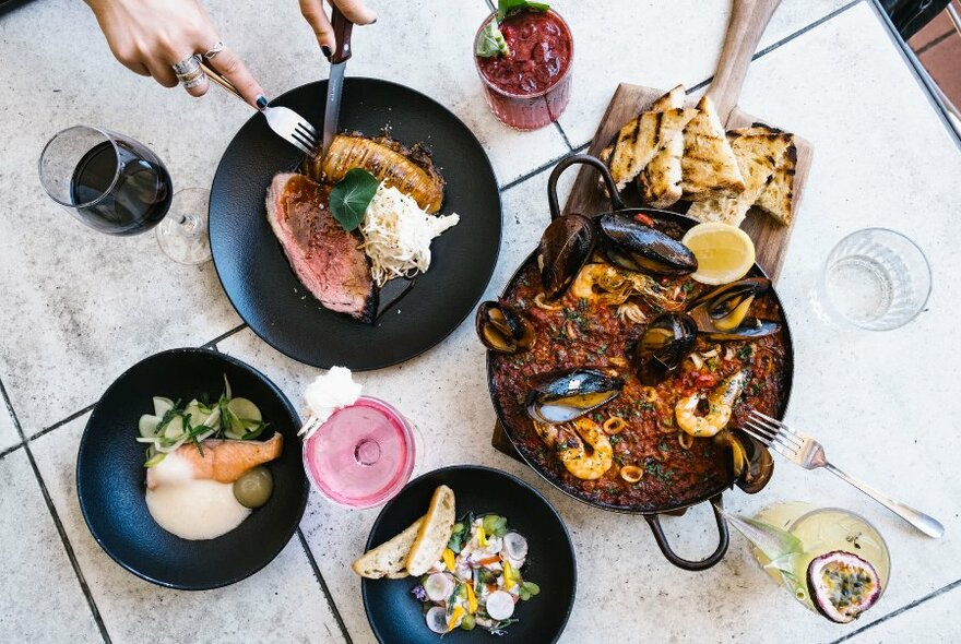 Overhead view of dishes of food on a table, with hands carving meat.