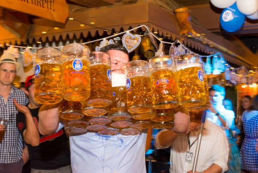 Man holding many many steins of beer in a pub setting.