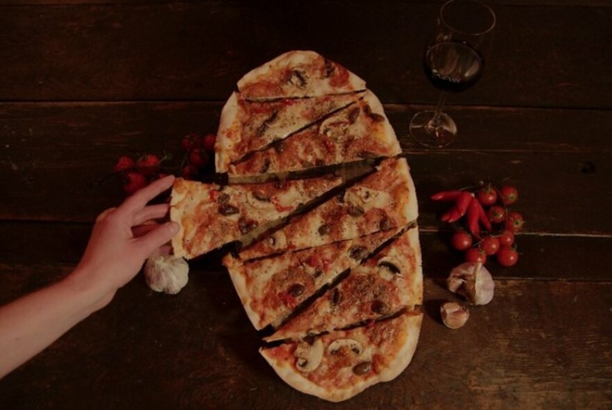 Person taking a slice from an oval-shaped pizza.