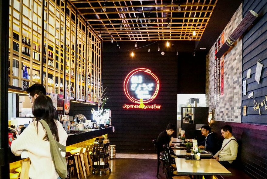 People seated at tables in a Japanese izakaya bar.