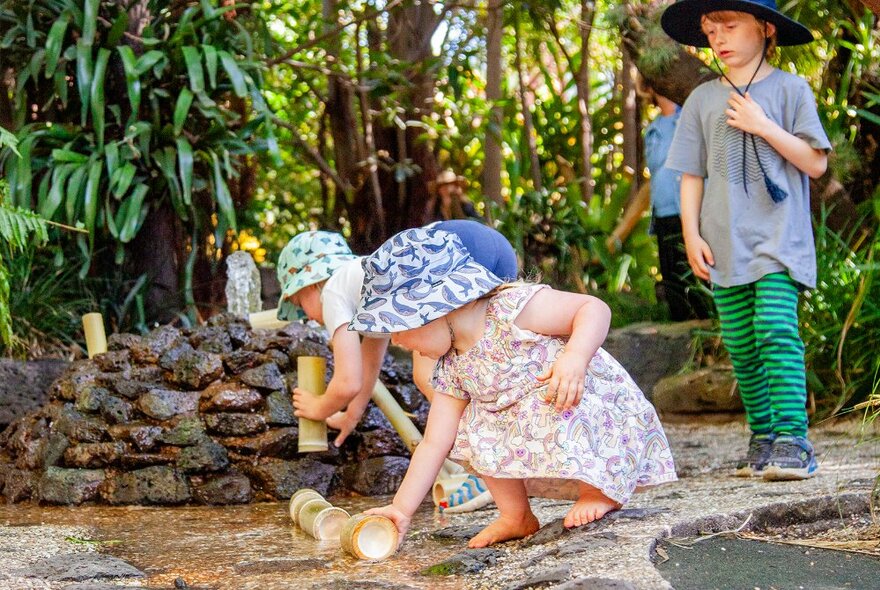 Young children playing outdoors in a garden and interacting with objects and water. 