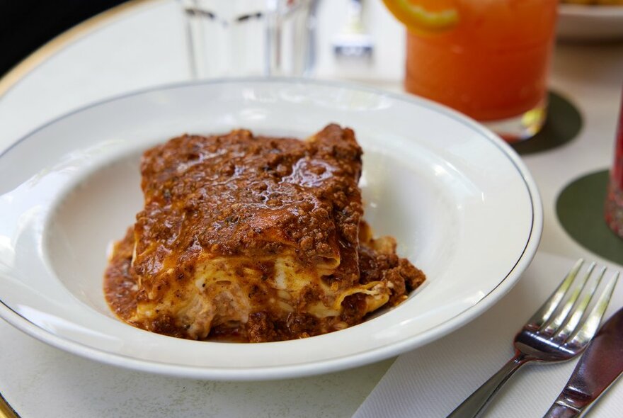 A slice of lasagne on a white plate covered in meat sauce.