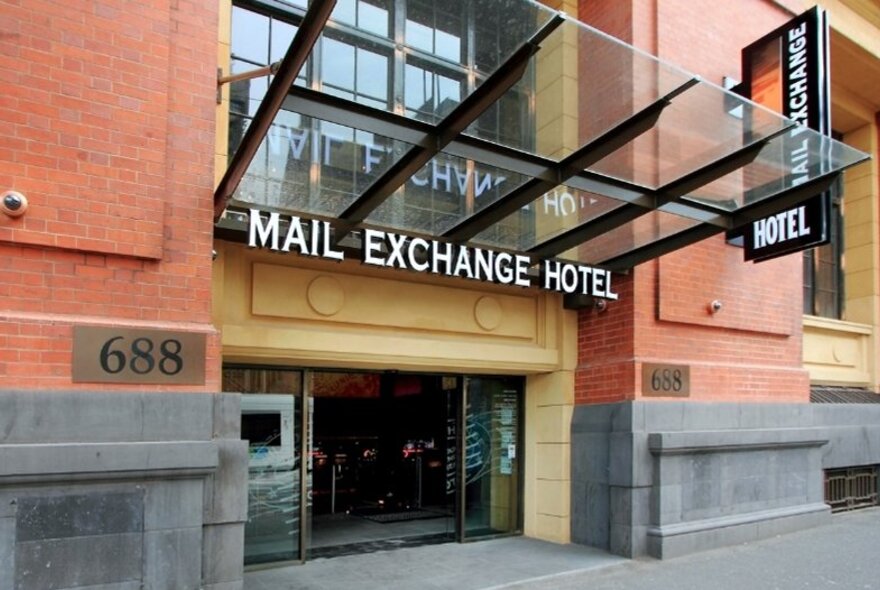 The exterior of the Mail Exchange Hotel with peach coloured stone and bluestone base and a clear annex over the doorway.