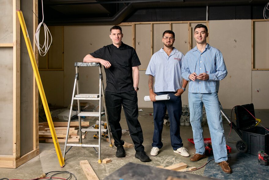 Three men in a restaurant undergoing renovation with ladder, exposed wires and tools.
