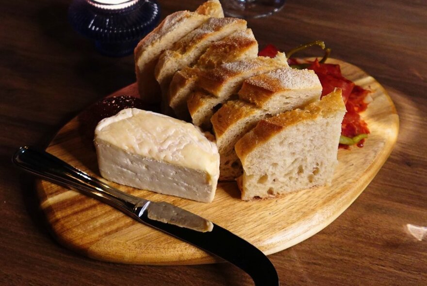 Round wooden platter with cheese, bread and knives.