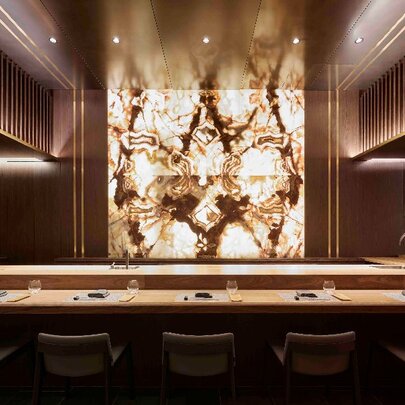 Five high stools facing a bar area that is set for meals, with an illuminated central wall facing the seats.