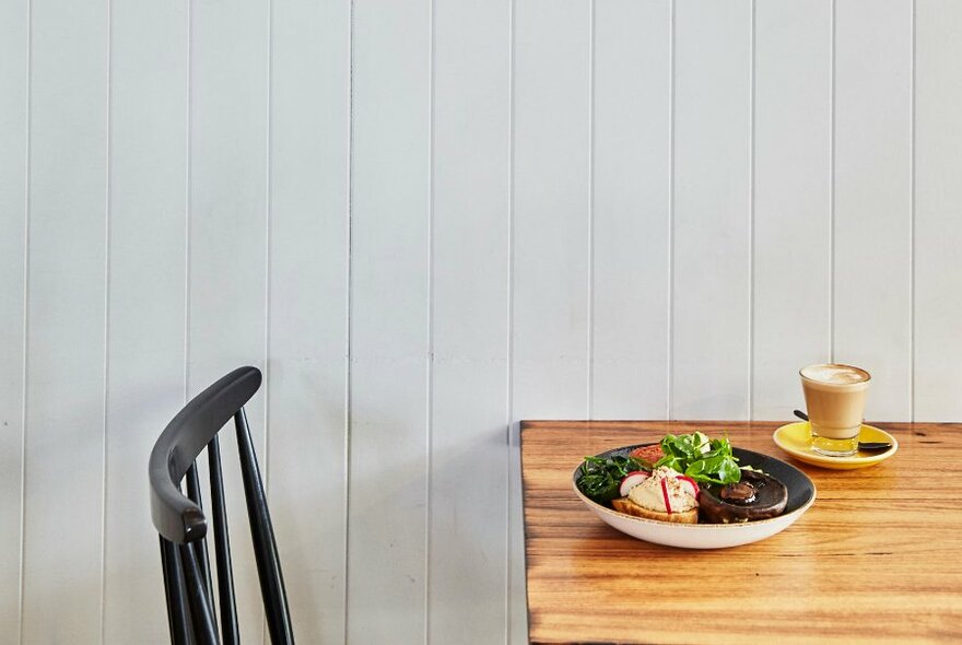 A chair at a table with a plate of food and cup of coffee on it.