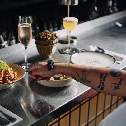 A sleek stainless steel bar counter with drinks, small dishes, and a person's arm at Lexy Restaurant and Bar.