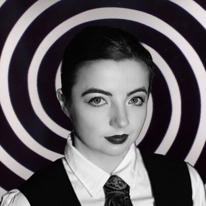 Woman wearing a tie and waistcoat with heavy makeup, black and white circles behind her.
