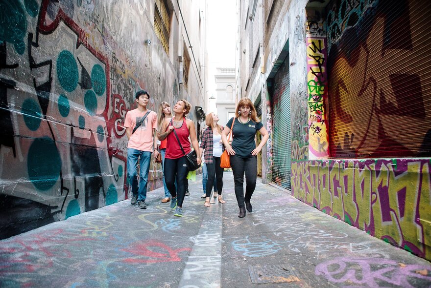A group of people being guided on a walk down one of Melbourne's bluestone laneways with street art on the walls.
