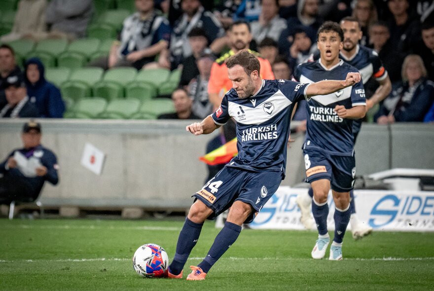 A soccer player kicks a ball with other players watching behind. 
