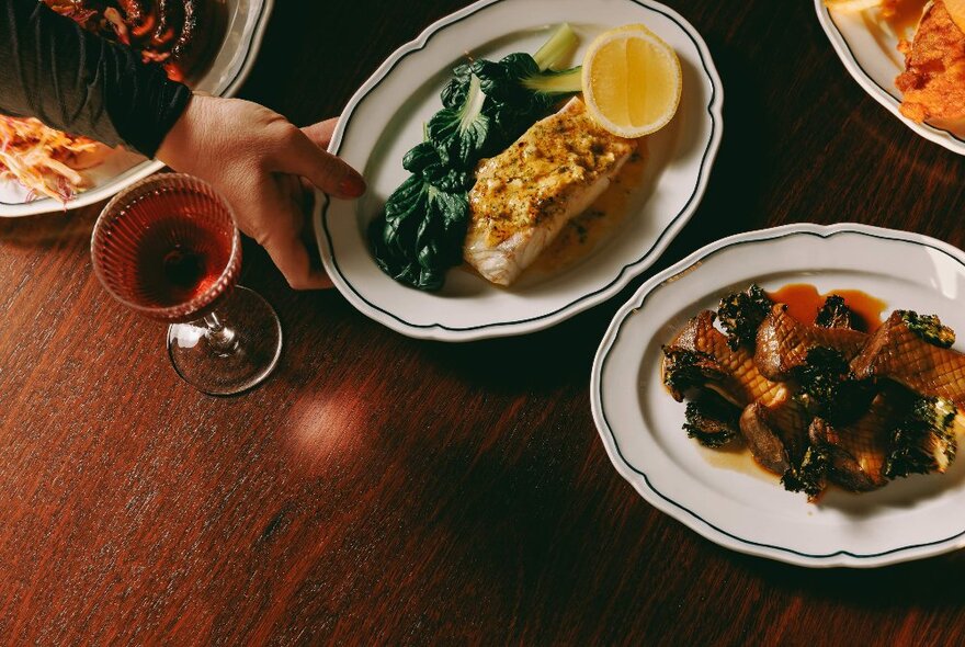 Dishes of elevated pub fare, with a glass of wine, presented on a dark wooden table.