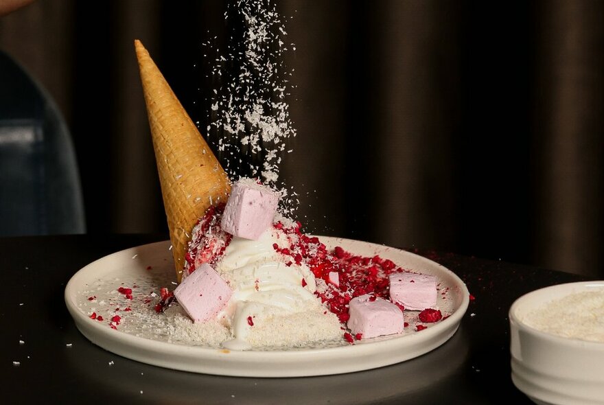 A dessert plate of an upside down icecream in a cone, with other sweet garnishes on top of it.