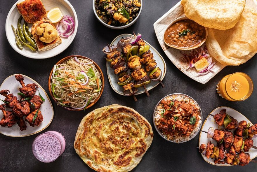 Array of Indian dishes on a wooden table, including breads, skewers and curries. 