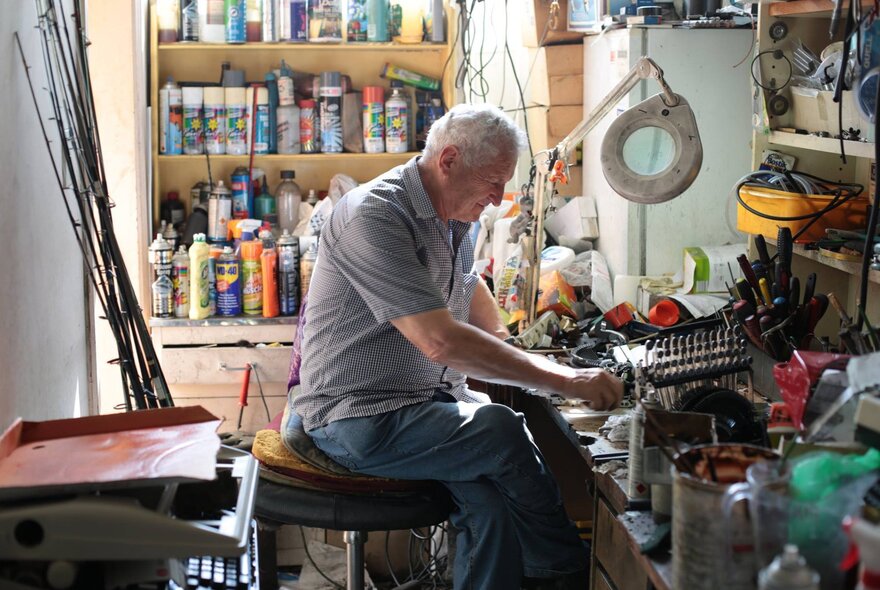 A man seated on a stool in a workshop.