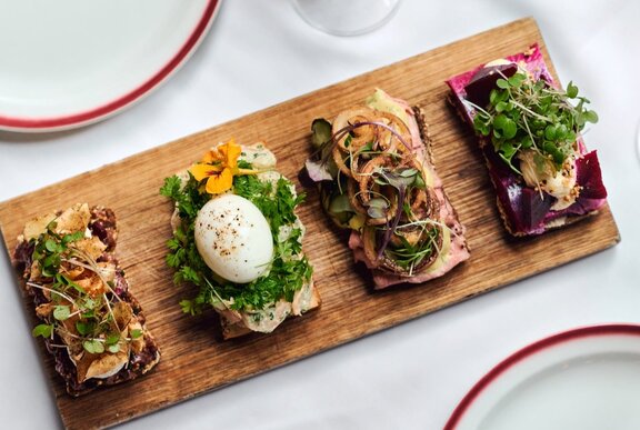 four open sanwiches with betroot and sprouts, pickles and onions, parsley and boiled eggs on a wooden serving board