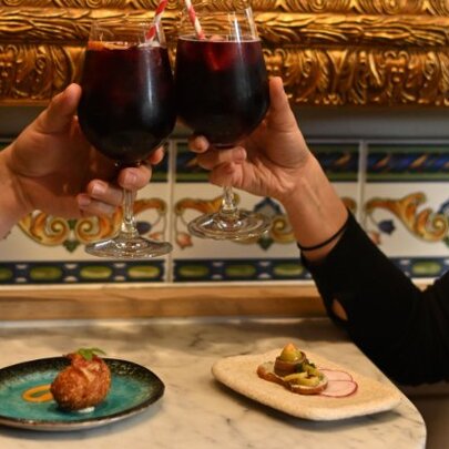 Hands clinking glasses of sangria at a marble restaurant table, with tapas.