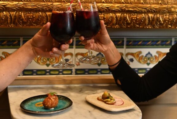 Hands clinking glasses of sangria at a marble restaurant table, with tapas.