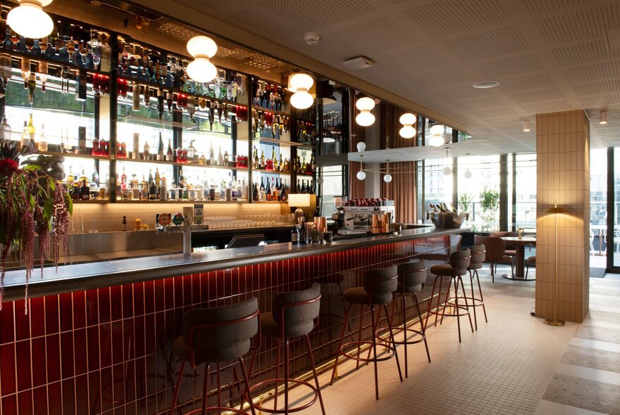 A long bar in hotel with curved stools and overhead lights. 