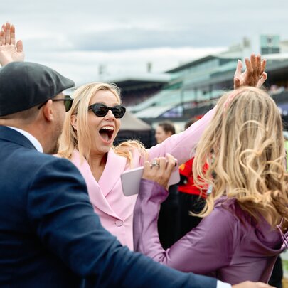 People celebrating with raised arms and screams at the races.