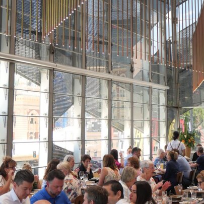 Airy dining space at Taxi Kitchen, with huge windows and overhead lighting, and patrons seated at tables eating and drinking.