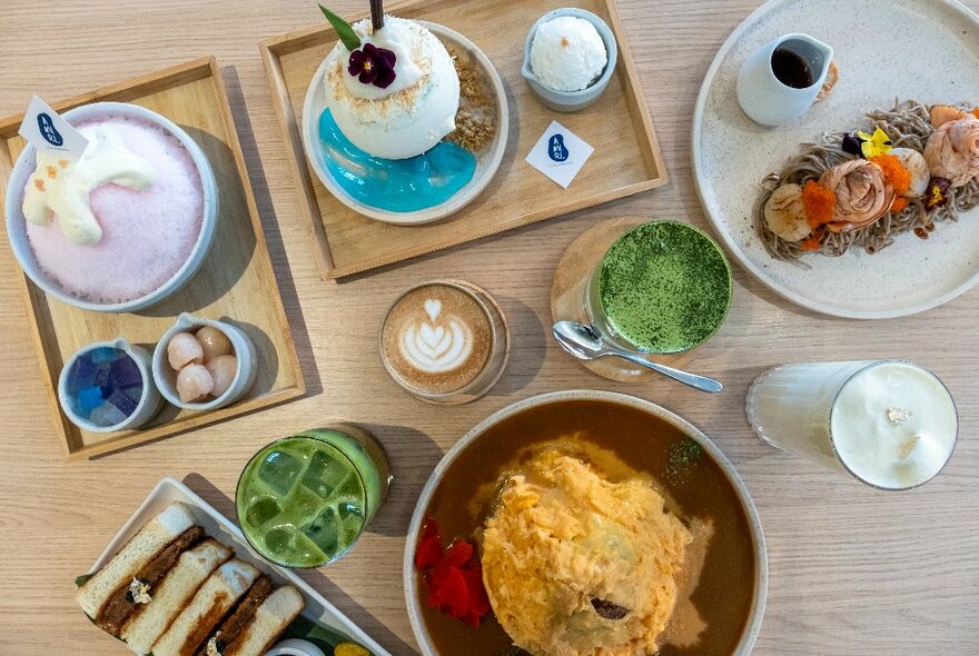 Looking down on a table with a wide variety of dishes including a sando, eggs, and desserts with matcha tea and coffee. 