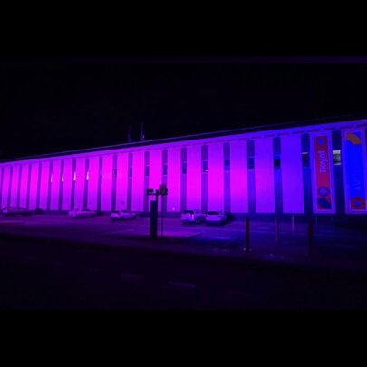 The external facade of a long building lit up purple at night.