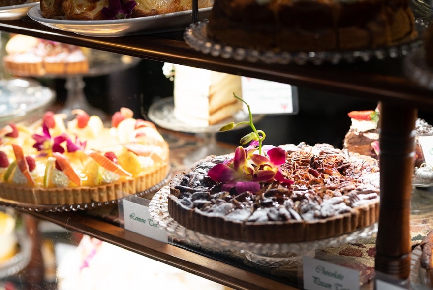 Close-up of two elaborate looking cakes on glass serving platters in a cafe window display.