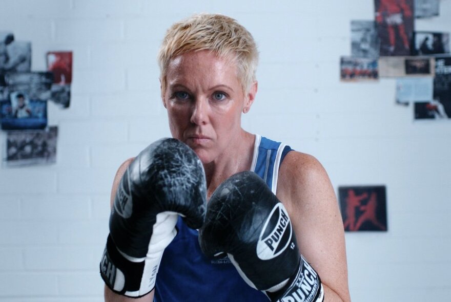 A still from the movie, Left Write Hook, with a blonde woman in a boxing stance wearing boxing gloves.