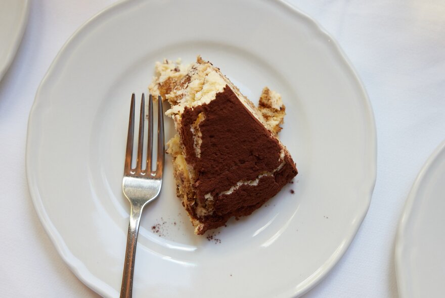 A slice of tiramisu on a white plate with a silver fork.