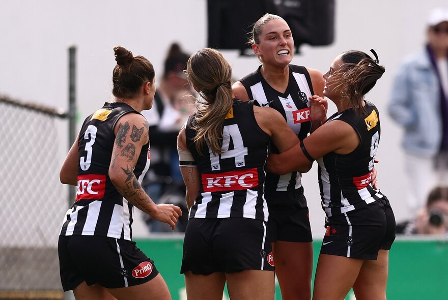 Collingwood AFLW players embrace in celebration on the field. 