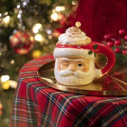 A frothy cocktail presented in a cute santa mug, resting on a tartan covered table with christmas lights in the background.