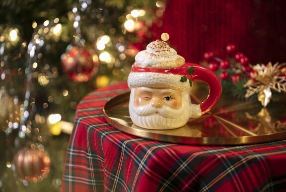 A frothy cocktail presented in a cute santa mug, resting on a tartan covered table with christmas lights in the background.