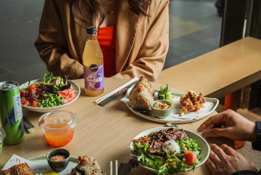 A person sitting at a cafe bench with dishes of salad, drinks and chopsticks.