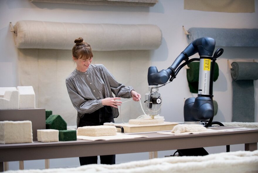 Designer Christien Meindertsma standing at a work table with a machine in front of her and making products out of waste wool material.