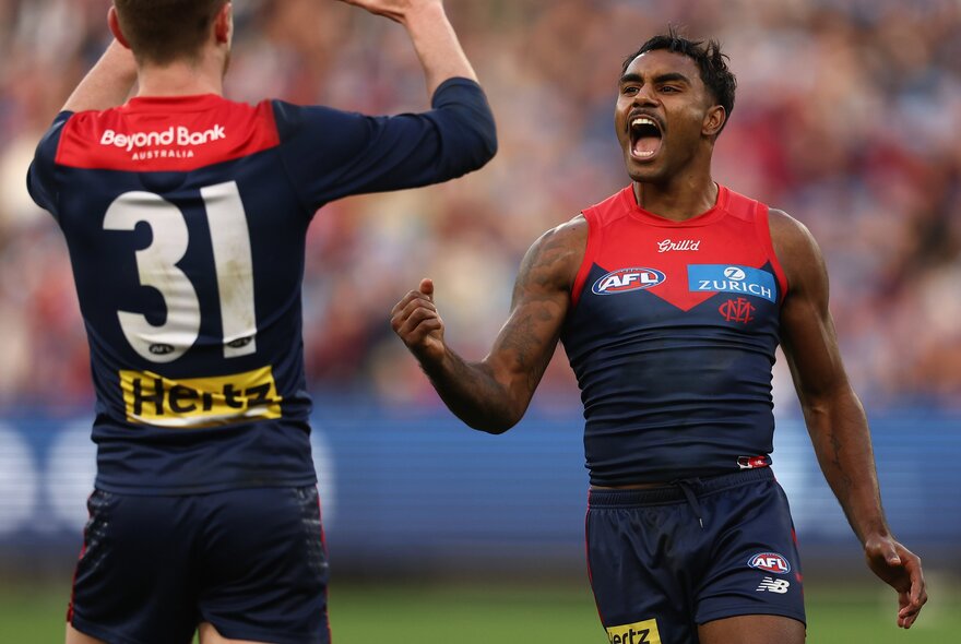 Two Melbourne AFL players cheering each other on a sports field.