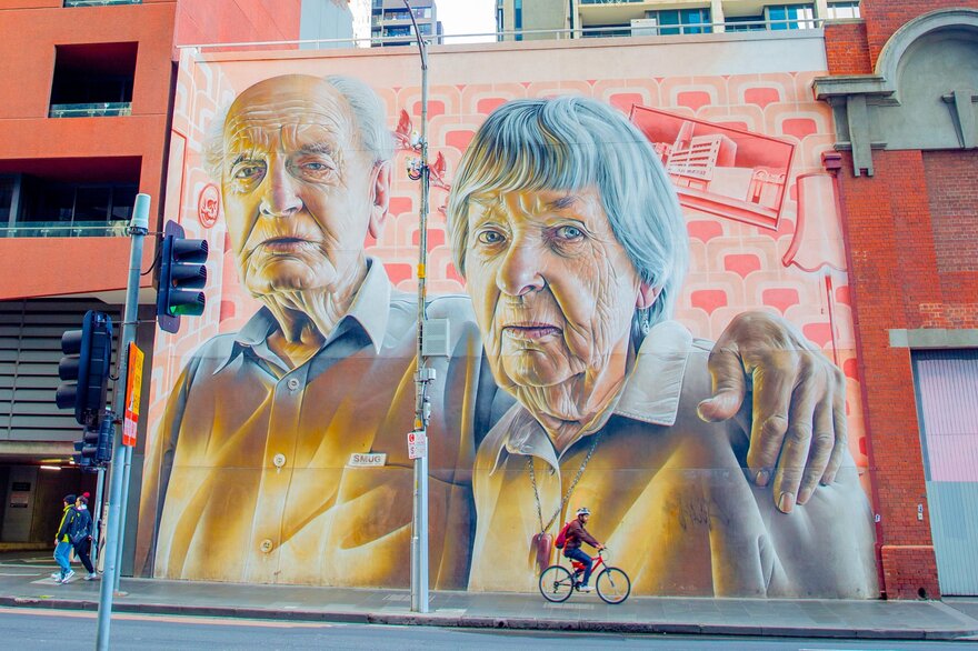 A large street art mural of two elderly people 