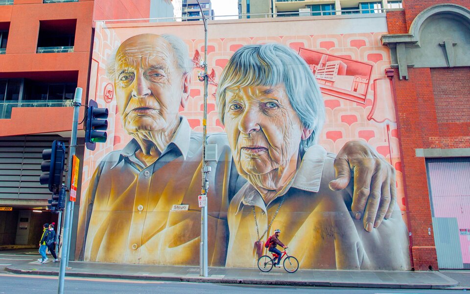 A large street art mural of two elderly people 