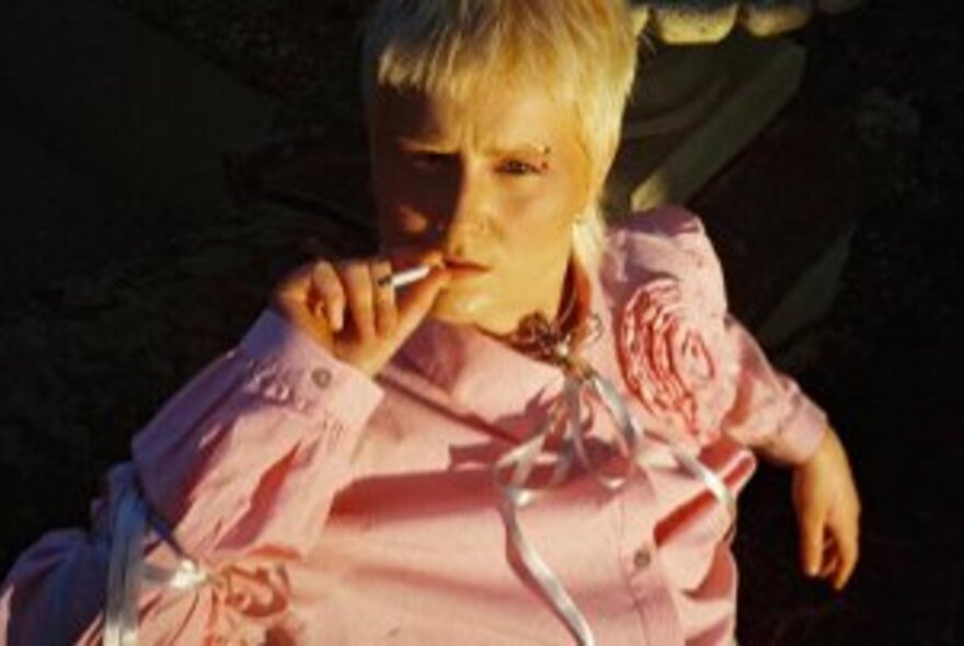 Performer with white-blond hair wearing a pink shirt with white ties.