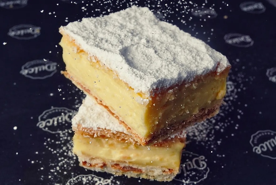 A custard filled flakey pastry, covered in icing sugar.