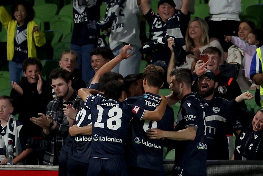 Melbourne Victory players embrace in front of their fans at a match. 
