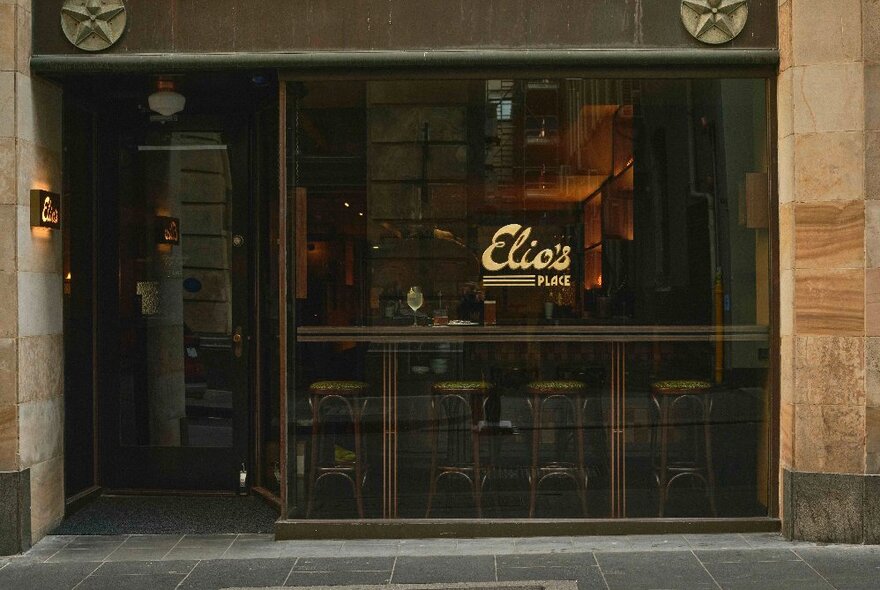 The shopfront of Elio's Restaurant, with golden signage and barstools in the window.