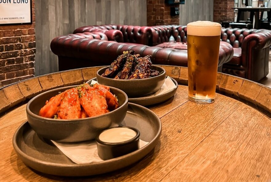 Plates of food on a table with a glass of beer, and Chesterfield leather couches in the background.