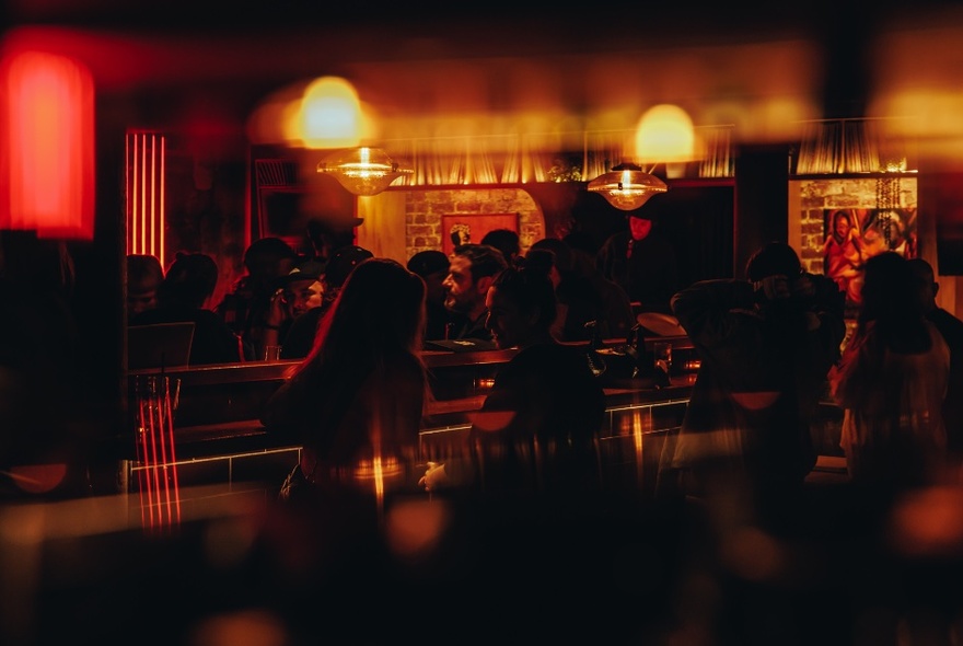 Dimly lit bar interior, with patrons standing at a bar.