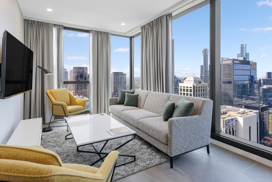 A hotel suite with sofa and chairs, a city view from the window. 