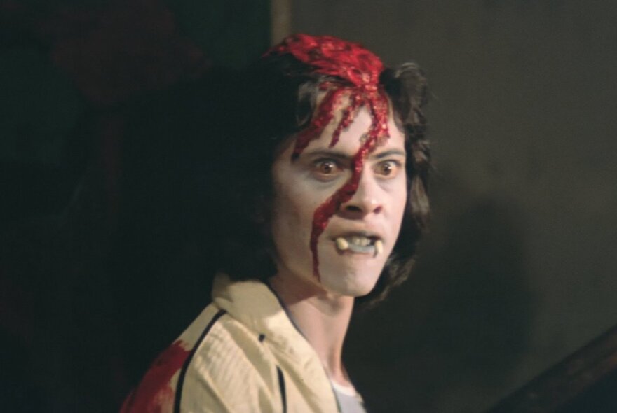 A still from an Indonesian horror film showing a man with blood pouring down his face from a gruesome wound on his head.